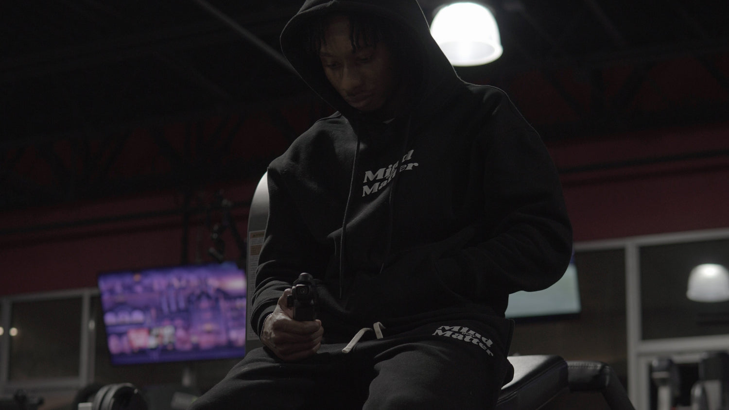 Person sitting on a chair in a dimly lit room with a television screen in the background.